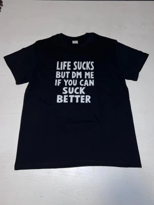 ”Life sucks but dm me if you can suck better” T-shirt - Svart T-shirt med kaxigt statement som garanterat drar blickarna till sig. Perfekt för dig med humor, attityd och självdistans. Bekväm passform och tydligt tryck – en tröja som säger det du tänker, högt och tydligt.