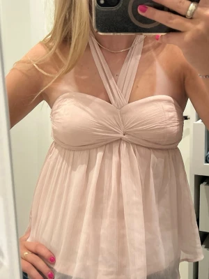 Ljusrosa halterneck topp - Supersöt ljusrosa topp med omlottband som knyts i nacken. Luftigt, plisserat tyg och vadderad byst ger en romantisk vibe. Perfekt till jeans eller kjol för en chic look. Materialet känns lätt och flowy, och toppen har en snygg twist framtill. Passar Xs