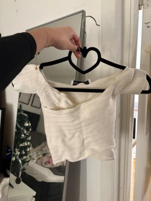 Vit ribbad offshoulder topp Bershka - Säljer en vit ribbad offshoulder topp från Bershka. Toppen har en croppad passform och är tillverkad i ett mjukt stretchigt material. Perfekt till jeans eller kjol för en trendig look. Har aldrig använt denna tröja pga av att den är för liten.