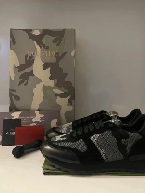 Valentino Rockrunner sneakers camo - Snygga Valentino Rockrunner sneakers i svart, grått och vitt med camouflage-mönster. Skorna har svarta snören, platt sula och detaljer i mocka och mesh. Perfekta för dig som vill sticka ut med exklusiva och trendiga sneakers.
