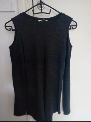 Mörkgrå offshoulder topp - Säljer en mörkgrå topp med offshoulder-detalj på ena axeln. Toppen har lång ärm på ena sidan och ärmlös på andra, vilket ger en cool asymmetrisk look. Materialet är mjukt och stretchigt, perfekt för dig som gillar stilrena och unika plagg.