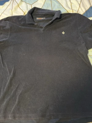 Svart pikétröja från Morris XL - Klassisk svart pikétröja(t shirt) från Morris i storlek XL. Tröjan har krage, kort ärm och en liten broderad logga på bröstet. Perfekt för en stilren och enkel look. Tillverkad i mjukt bomullsmaterial. Använt ett fåtal gånger, nypris ca 1000 säljer för 500 för vill inte ha den skräpandes hemma