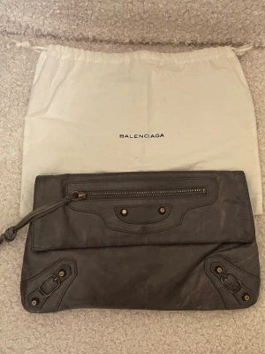 Balenciaga leather clutch bag - Säljer min gråa Balenciaga leather clutch bag i grått som jag köpt på vestiare. Mått 30x 18 cm. Bra skick förutom tassels som är lite i använt skick. Annars inga skador. Kan skicka fler bilder vid intresse. Pris är diskuterbart vid smidig affär.