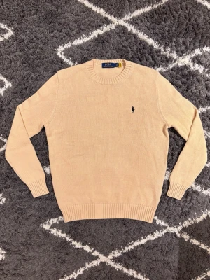  Polo Ralph Lauren tröja  - Säljer en beige stickad tröja från Polo Ralph Lauren med klassisk rund hals och svart broderad logga på bröstet. Tröjan har ribbade muddar vid ärmslut och nederkant, Jag väger 70KG och är 180CM och den passar mig perfekt.