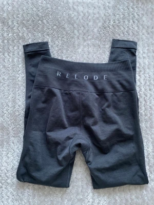 Mörkgrå leggings från Relode XXS - Supersnygga mörkgrå leggings från Relode i storlek XXS. De har hög midja och bred resår med logga framtill. Materialet är stretchigt och mjukt, perfekt för träning eller chill. Sitter tight och formar sig efter kroppen.