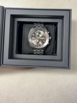 Stilren silverfärgad BOSS klocka - Säljer en snygg och stilren klocka från BOSS i silverfärgat rostfritt stål. Klockan har en klassisk länkarmband, kronograf-funktion och datumvisning. Kommer med originalbox, extra länkar och svart BOSS-påse. Perfekt accessoar för dig som gillar en clean look. Använd 1 gång 