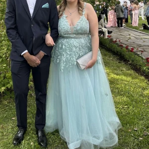 Ljusblå glittrig balklänning med blommor - Superfin ljusblå balklänning med blommiga och glittriga detaljer. Djup v-ringning, snörning i ryggen med dragkedja. Perfekt för bal! Endast använd 1 gång. Inget synligt smuts. Storlek 12, den är från Zapaka. Hör av dig om du har frågor eller funderingar, fler bilder kan skickas! Ordinarie pris är 1300 kronor. Köparen står för frakten. 