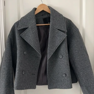 Grå skepparkavaj från 157, XS - Stilren grå skepparkavaj från 157 i kort modell med bred krage och dubbelknäppning. Jackan är fodrad och har klassiska knappar framtill. Perfekt för dig som gillar en clean och tidlös look. Extra knapp medföljer. Helt ny aldrig använt! 