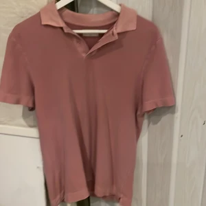 Rosa pikétröja från These Glory Days - Säljer en stilren rosa pikétröja från These Glory Days i storlek small. Tröjan har klassisk krage, korta ärmar och knäppning framtill. Materialet är mjuk bomull som känns skönt mot huden. Perfekt för dig som gillar enkel och snygg design. Tveka inte att höra av dig vid frågor.