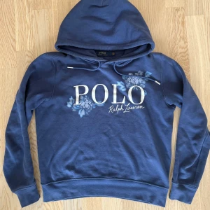 Blå hoodie från Polo Ralph Lauren - Blå hoodie från Polo Ralph Lauren med stor vit logga och blommigt tryck framtill. Tröjan har huva med snörning och långa ärmar. Mjuk bomullskvalitet som är skön att bära. En av dom fetaste från Ralph Lauren. Skick 8/10 storlek S💫 För fler frågor kom pm/ Neo💫