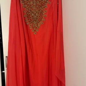 Stark rosa långklänning med glittriga detaljer - Säljer en rosa  långklänning med vackra glittriga gulddetaljer och pärlor framtill. Klänningen har en luftig och svepande passform, perfekt för att sticka ut. Materialet känns lätt och elegant, och designen är riktigt iögonfallande.