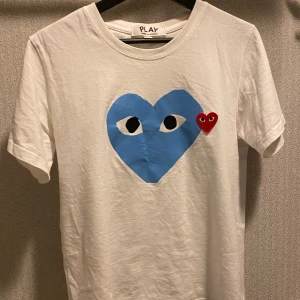 Vit  Play t-shirt - Säljer en vit t-shirt med det ikoniska blå hjärtat med ögon och ett litet rött hjärta på bröstet. T-shirten är i bomull och har en klassisk passform med korta ärmar. Perfekt statement-plagg för dig som gillar streetstyle. Pris kan diskuteras 🙌