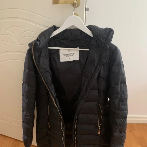 Svart pufferjacka Chiara Forti Milano - Svart pufferjacka från Chiara Forti Milano med huva och guldiga dragkedjor. Jackan är quiltad och har två fickor framtill med dragkedja. Perfekt för kalla dagar och har en snygg, enkel design som funkar till det mesta. Storlek 34, pris 300🩷