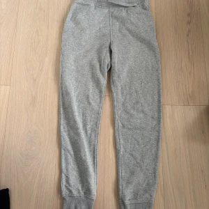 Grå mjukisbyxor från H&M - Grå mjukisbyxor från H&M med resår i midjan och muddar vid bensluten. Byxorna är tillverkade i mjukt material och har en enkel, klassisk design som passar perfekt för chill dagar eller när du vill vara bekväm.