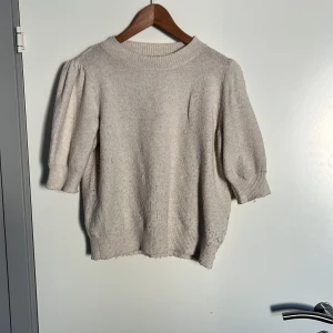 Beige stickad tröja Vero Moda S - Beige stickad tröja från Vero Moda med korta puffärmar och rund halsringning. Tröjan har ribbade muddar vid ärmslut och nederkant, vilket ger en snygg och trendig look. 