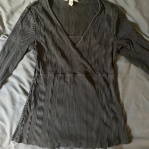 Svart omlottopp med ribbad struktur - Svart omlottopp från H&M med lång ärm och ribbad struktur. 