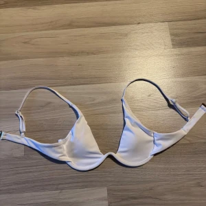 Vit bikiniöverdel med bygel - Snygg vit bikiniöverdel med bygel och justerbara axelband. Enkel och stilren design som passar perfekt till stranden eller poolen. Ger bra stöd och har en klassisk form. Perfekt för dig som gillar en clean look på sommaren.