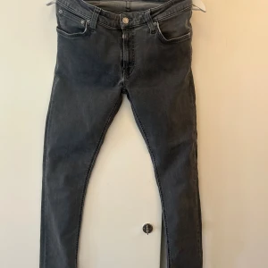 Grå skinny jeans från Nudie Jeans - Snygga grå jeans från Nudie Jeans i modellen skinny fit. Klassisk femficksdesign, smal passform och stretchigt jeanstyg som sitter tajt hela vägen ner. Perfekta för dig som gillar en stilren och modern look. Köpta på NK för 1799kr. Säljer då jeansen är för små, dem är använda men är i bra skick!
