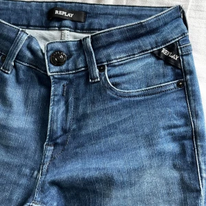 Blå jeans från Replay - Snygga blå jeans från Replay med klassisk femficksdesign och diskret slitning. Jeansen har smal passform, normal midja och är tillverkade i stretchigt denim för extra komfort. Svarta detaljer på bakfickan och Replay-logga vid fickan framtill.
