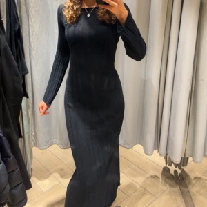 Svart lång stickad klänning med öppen rygg - Säljer en svart lång stickad klänning med figurnära passform och lång ärm. Klänningen har en snygg öppen detalj i ryggen som ger en extra touch. Jag är 175 för referens. Använd en gång