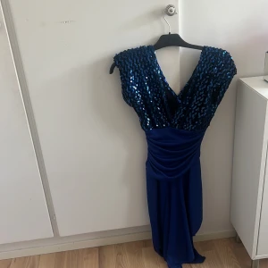 Blå långklänning med paljetter från Climax - Snygg vintage blå långklänning från Climax by David Howard med glittriga paljetter upptill och djup v-ringning. Klänningen har draperad midja och är ärmlös, perfekt för dig som vill sticka ut med en glamorös look.