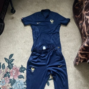 Frankrike Nike fotbollströja marinblå M - Säljer en officiell Frankrike fotbollströja från Nike i marinblått med guldiga detaljer och FFF-logga. Tröjan är kortärmad, har diskret mönster och är tillverkad i Dri-Fit material som andas. Slim fit-modell, perfekt för dig som gillar sportig stil.