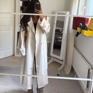 Beige trenchcoat från H&M - Snygg beige trenchcoat från H&M med klassisk krage, dubbelknäppning och axelklaffar. Aldrig använd. Storlek XS. 600 kr