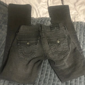 Svarta True Religion jeans, stl 24 - Snygga svarta jeans från True Religion med ikoniska broderade bakfickor och silverfärgade knappar. 