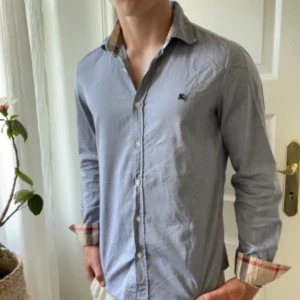 Burberry skjorta  - Väldigt snygg färg, grå / blå. Storlek M och modellen är 180,75 kg. Inga defekter förutom en liten fläck som ni ser på sista bilden på högra bröstet. 