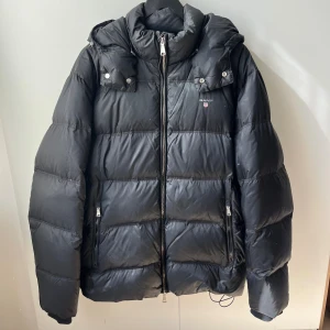 Gant Jacka - Säljer denna Gant Jacka i storlek L modell ”The Alta Down Jacket”.  Jackan är otroligt tjock i material och går att spännas åt nedtill, för att få en mer slimmed look, men även vid luvan. Finns inga tecken på skador. Pris kan diskuteras vid snabbköp.