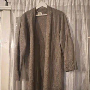 Beige lång kofta från H&M XS - Lång, öppen beige kofta från H&M i storlek XS. Koftan har ribbade muddar vid ärmsluten och är stickad i ett mjukt material. Perfekt för lager-på-lager och chill dagar. Enkel och stilren design som passar till det mesta.