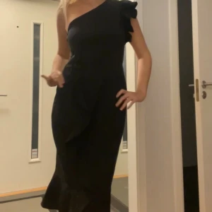 Svart oneshoulder långklänning - Jätte fin klänning, off shoulder. Använd en gång. Bilderna är tagna från en video så lite suddiga, kan skicka flera om behövligt. Har väldigt fin passform och slits fram vid benet