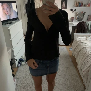 Svart långärmad omlottopp med öppen rygg - Svart långärmad topp med djup v-ringning och omlottdesign. Toppen har öppen rygg med knytband och sitter snyggt figurnära. Perfekt för dig som gillar trendiga och stilrena plagg med det lilla extra. Xs/s