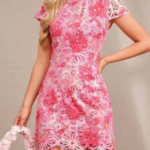 Rosa blommig spetsklänning - Superfin kort klänning i rosa och vit med blommigt spetsmönster. Klänningen har korta ärmar, rund hals och figurnära passform. Materialet är spets med broderade blommor som ger en unik och fräsch look. Perfekt för sommarens alla tillfällen!