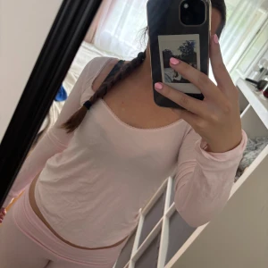 Ljusrosa långärmad topp - Säljer en söt ljusrosa långärmad topp med rundad halsringning och diskret spetskant. Toppen är i mjukt material och har en slim passform som sitter snyggt på kroppen. Perfekt för dig som gillar en enkel men gullig stil.