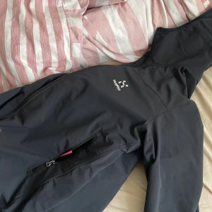 Svart vindjacka från Haglöfs strl S - Säljer en svart vindjacka från Haglöfs i storlek S. Jackan har huva, långa ärmar med resår vid mudden och praktiska fickor med dragkedja. Perfekt för utomhusaktiviteter och har en stilren design med diskret logga på bröstet.
