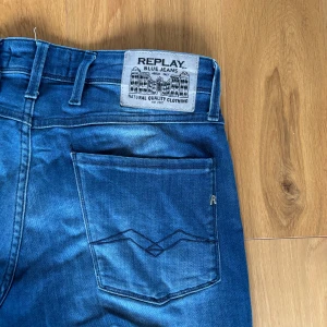 Replay Anbass slim fit jeans blå - Säljer ett par Replay Anbass slim fit jeans i klassisk blå tvätt. Jeansen har fem fickor, snygga detaljer på bakfickan och en bekväm passform som sitter tajt men ändå flexar. Perfekta för dig som gillar stilrena och moderna jeans. 