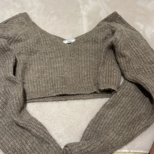 Beige stickad croppad tröja Gina Tricot - Supermysig beige stickad tröja från Gina Tricot med v-ringning och croppad passform. Tröjan har långa ärmar och är perfekt för lager-på-lager under höst och vinter. Ribbstickad struktur som ger en trendig och avslappnad look.