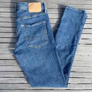 Blå slim jeans från Jack & Jones - Storlek 28/32. Snygga blå skinny jeans från Jack & Jones med klassisk femficksdesign och ljusbruna sömmar. Jeansen har en smal passform och är tillverkade i denim för extra komfort. 