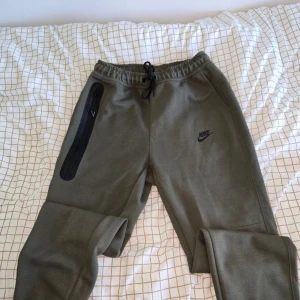 Olivgrön Nike Set L - Snygga olivgrön Nike set med storlek L men känns som M. Byxorna har elastisk midja med snörning, svarta Nike-loggor och en cool dragkedjeficka på benet. Luvtröjan är underbar med stora fickor och bra material. Tillverkade i mjukt material som är perfekt för chill eller träning.