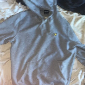 Grå hoodie från Lyle & Scott, storlek L - Säljer en stilren grå hoodie från Lyle & Scott i storlek L. Tröjan har klassisk huva med snörning, magficka och den ikoniska gula loggan på bröstet. Perfekt för chill dagar och enkel att matcha med jeans eller joggers.