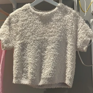 Beige fluffig kortärmad topp - Supermjuk och fluffig beige topp med korta ärmar och rund hals. Den är lite kortare om man vill visa pyttelite mage, annars tycker jag att det är väldigt snyggt med ett vitt linne under!