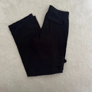 Svarta cargobyxor med raka ben - Svarta cargobyxor med raka ben och stora fickor på sidorna. Byxorna har bälteshällor och klassisk cargostil. Materialet känns mjukt och lätt, perfekt för en avslappnad look. Passar dig som gillar praktiska och stilrena byxor.