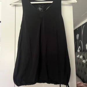 Svart linnetopp från Peak Performance - Svart linnetopp från Peak Performance med lös passform och rund halsringning. Toppen är ärmlös och har en sportig racerback-design. Tillverkad i ett lätt och svalt syntetmaterial, perfekt för träning eller aktiva dagar.