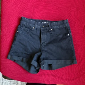 Svarta jeansshorts från FB Sister - Snygga svarta jeansshorts från FB Sister i klassisk femficksmodell. De har hög midja, uppvikta benslut och stängs med dragkedja och knapp. Perfekta till sommaren och lätta att matcha med allt. Materialet är mjukt och stretchigt för extra komfort.