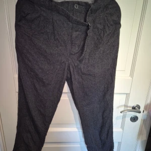 Grå kostymbyxor i ullmix Michael Kors  - Mörkgrå kostymbyxor i klassisk rak modell med  knappstängning. Byxorna är tillverkade i en mjuk ullmix med lite elastan för extra komfort. Perfekta för en clean och stilren look. Behöver strykas. Sambon upplever att dem är lite små i storleken.