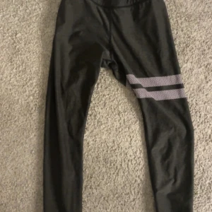 Svarta leggings med vita ränder - Snygga svarta leggings med två vita randiga detaljer på ena benet. Perfekta för träning eller chill, med stretchigt material som sitter skönt och följer kroppen. Enkel design som passar till det mesta.