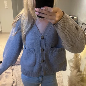 Brun stickad kofta med knappar - Mysig brun stickad kofta med v-ringning och stora träknappar framtill. Koftan har två rejäla fickor och en loose passform med långa ärmar.