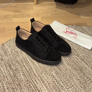 Christian Louboutin svarta sneakers med nitar - Svarta sneakers från Christian Louboutin i mocka med svarta nitar på tån och klassisk röd sula. Skorna har snörning och rund tå, samt en platt sula. Insidan är ljusbeige och sulan har Louboutins signatur. Riktigt edgy och lyxig vibe. Några defekter som inte syns på avstånd! Inga skambud tack! 920kr så får du en NK påse på köpet!