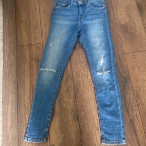 Blå skinny jeans från LAB Industries - Snygga blå skinny jeans från LAB Industries med slitna detaljer på båda benen. Klassisk femficksmodell med normalhög midja och smal passform. Jeansen är gjorda i hållbar denim och har en fräsch, modern look med dragkedja och knapp framtill. Pris kan diskuteras💕